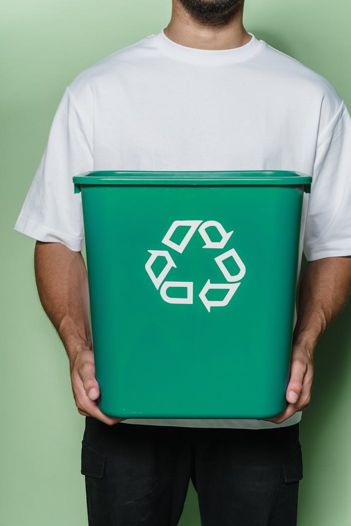 services-01 Adult male holding a green recycling bin against a green background, promoting sustainability.
