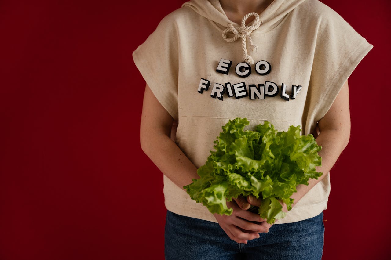hero-img-02 Woman in an eco-friendly hoodie holding fresh lettuce against a red background.